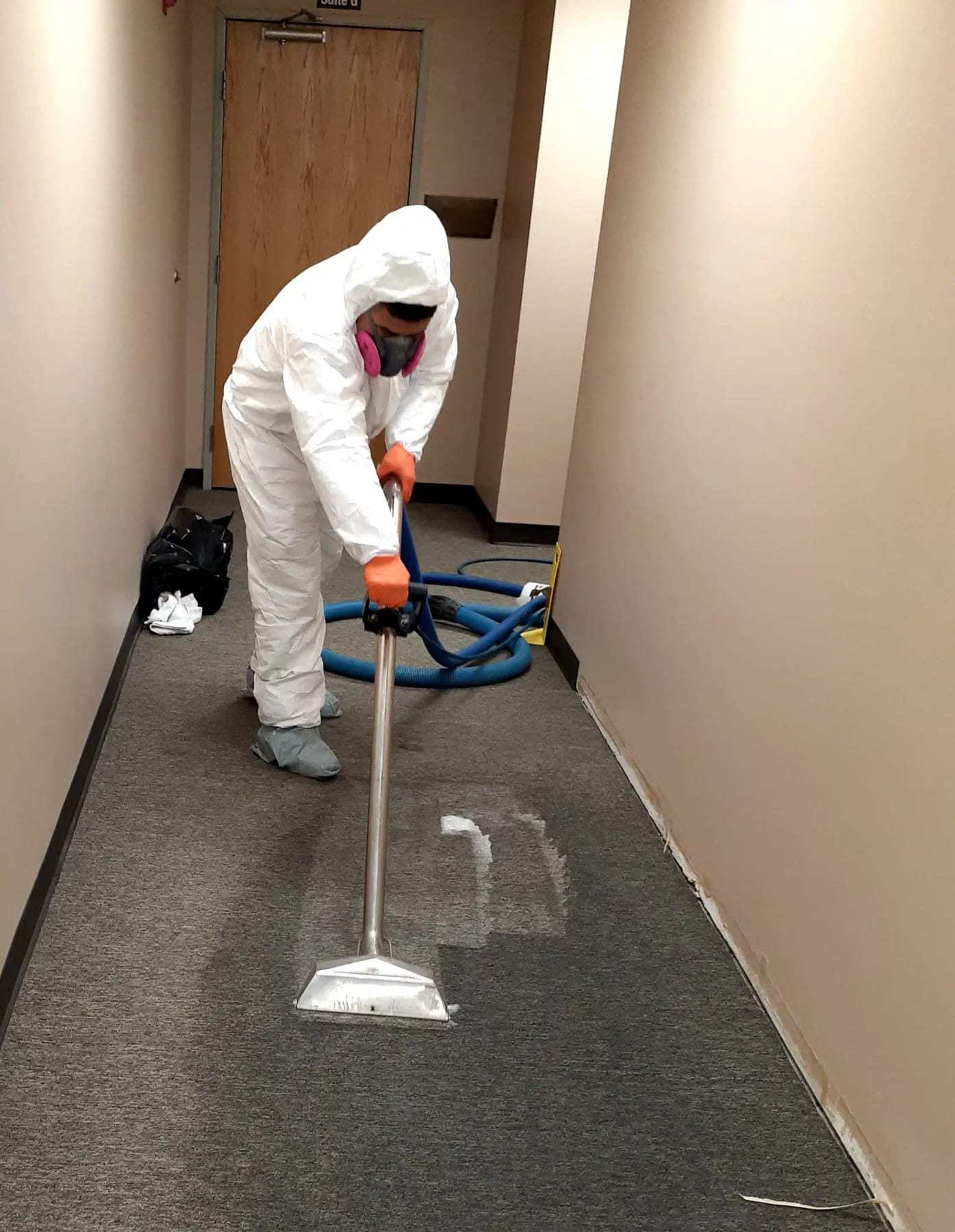Technician in a protective suit extracting water from carpet in a narrow corridor